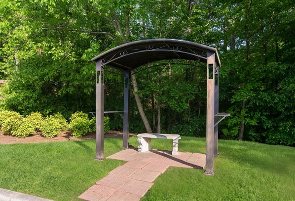 A gazebo with a bench, surrounded by grass and trees.