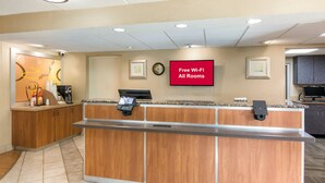A reception desk with a digital screen displaying 'Free Wi-Fi All Rooms' and a clock on the wall. - Red Roof Inn Durham - Triangle Park (Durham)