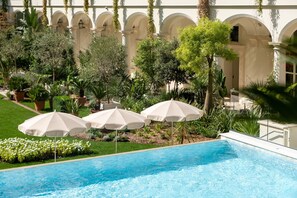 A swimming pool with three white umbrellas, surrounded by greenery and a building with arched windows. - Carlton Cannes, a Regent Hotel (Cannes)