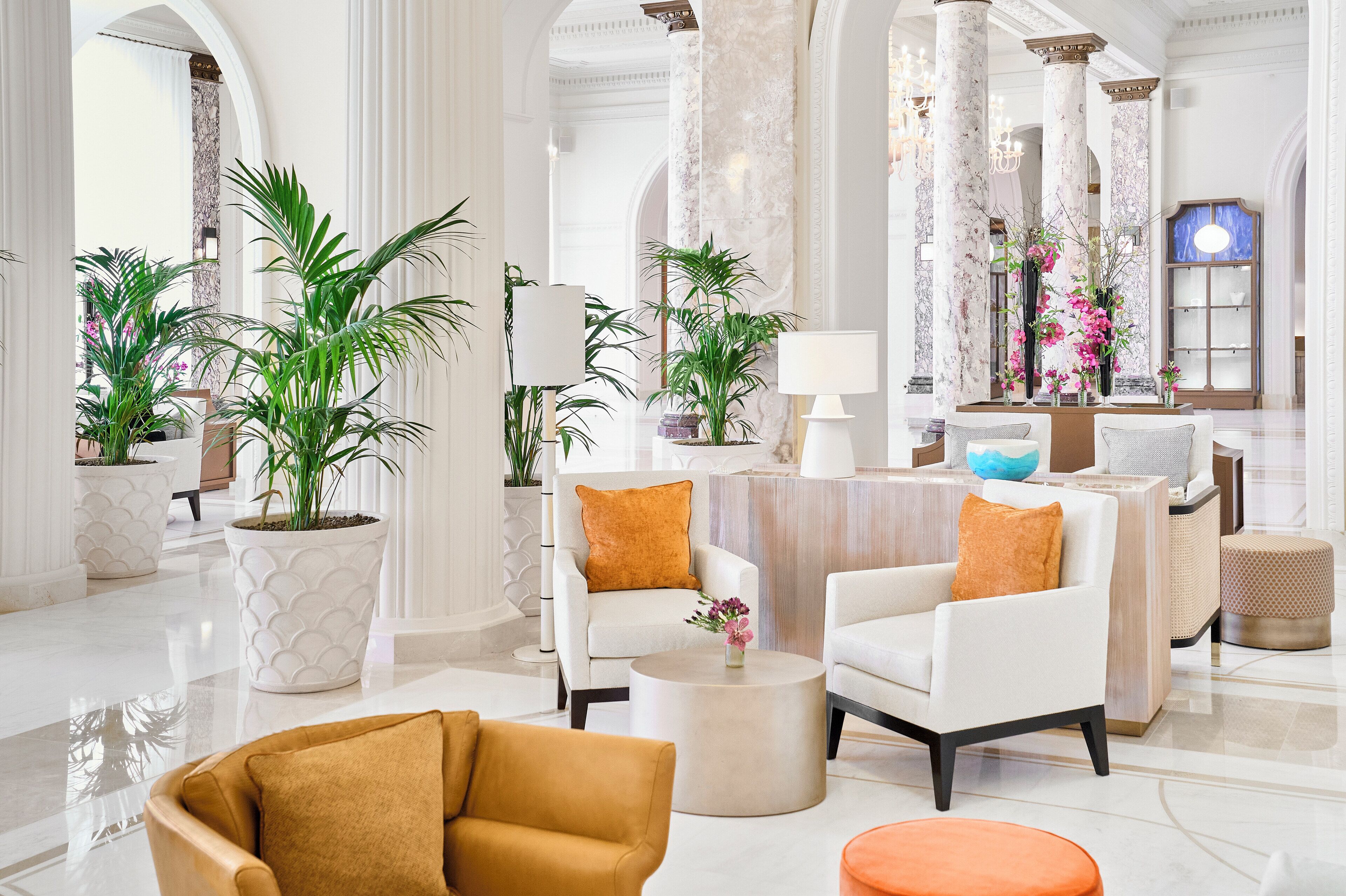 A spacious lobby with white armchairs, a round coffee table, and large potted plants.