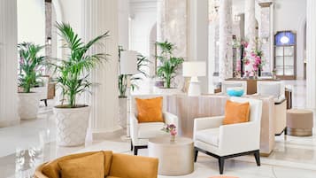 Eine geräumige Lobby mit weißen Sesseln, einem runden Couchtisch und großen Kübelpflanzen.