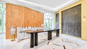 A modern hotel lobby with a large wooden herringbone wall, a glass-top table, and a large window with a view of greenery.