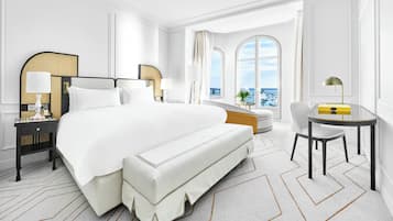 Amplia habitación de hotel con una cama grande, zona de estar y vistas al mar a través de amplios ventanales.