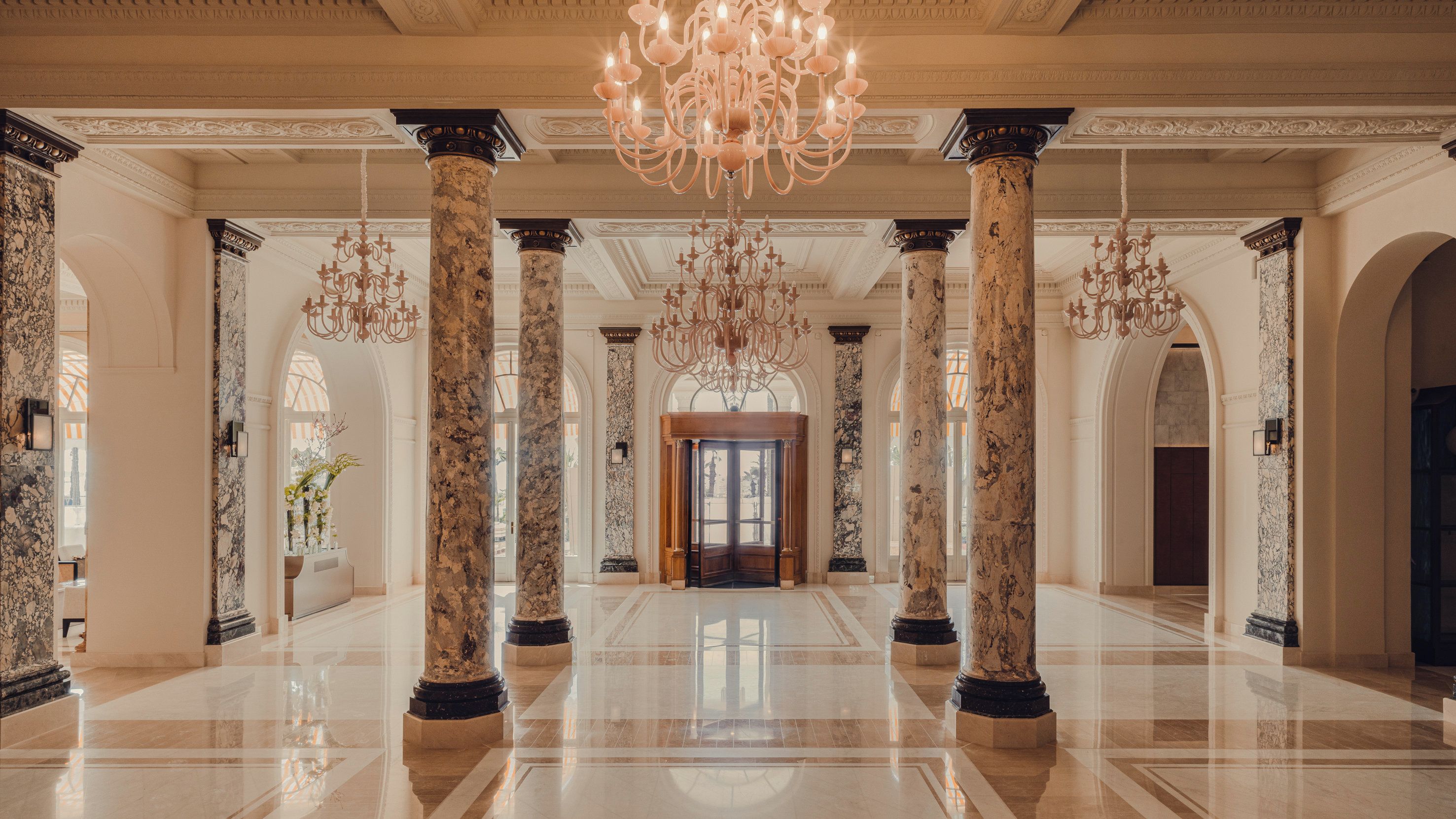 Un vaste hall d’entrée orné de colonnes de marbre, d’un grand lustre et d’une porte centrale.