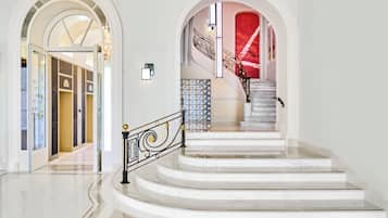 A grand staircase with marble steps and ornate black railings, leading to a red wall with stained glass windows.
