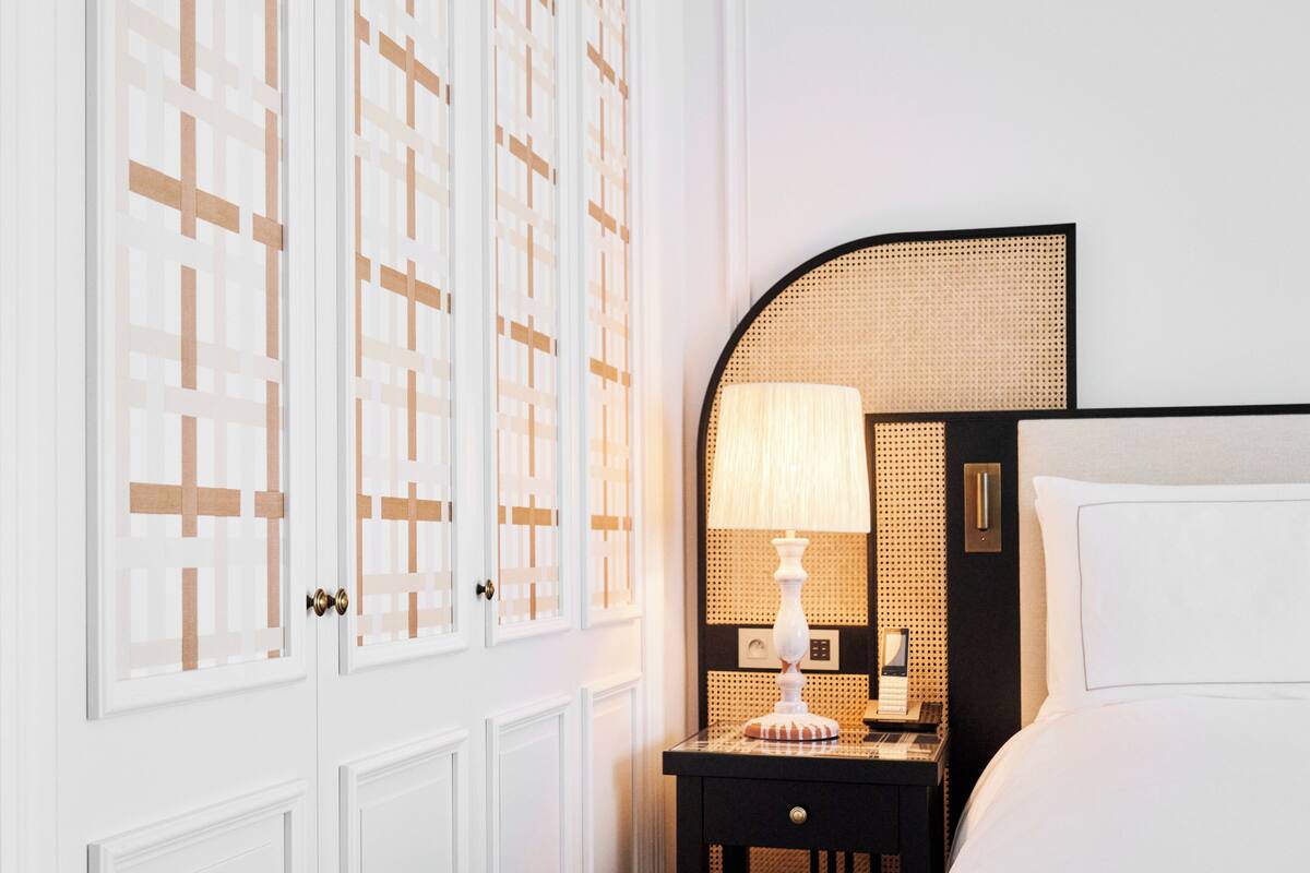 A hotel room with a bed, a nightstand with a lamp, and a wall with a geometric pattern.
