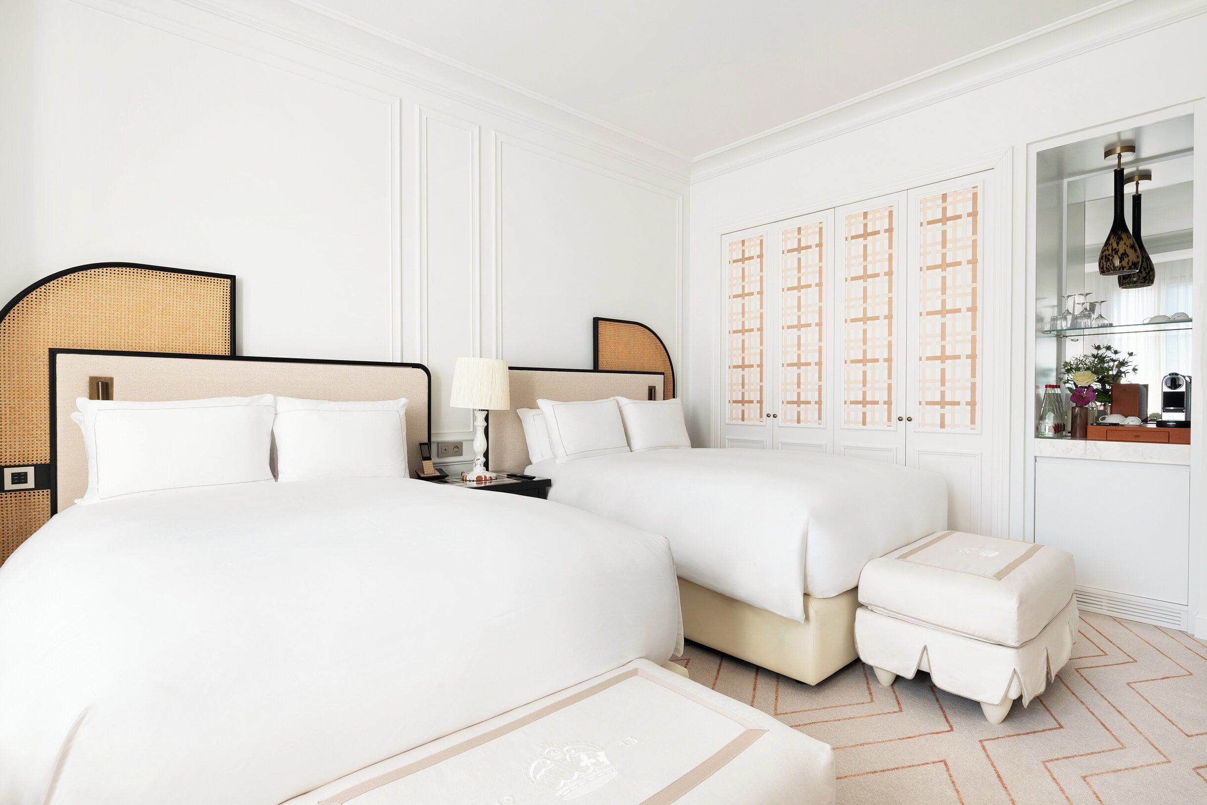 A hotel room with two beds, a nightstand, a lamp, a small table, and a decorative cabinet.