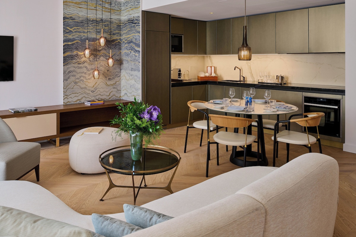 A modern living room with a sofa, a coffee table with a vase of flowers, and a dining area with a round table and chairs.