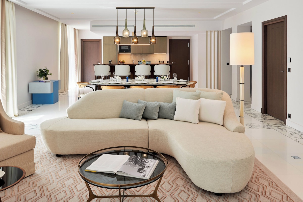A modern living room with a beige sofa, a coffee table, and a dining area in the background.