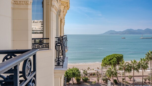 A balcony with ornate railings overlooking a beach and ocean. - Carlton Cannes, a Regent Hotel (Cannes)