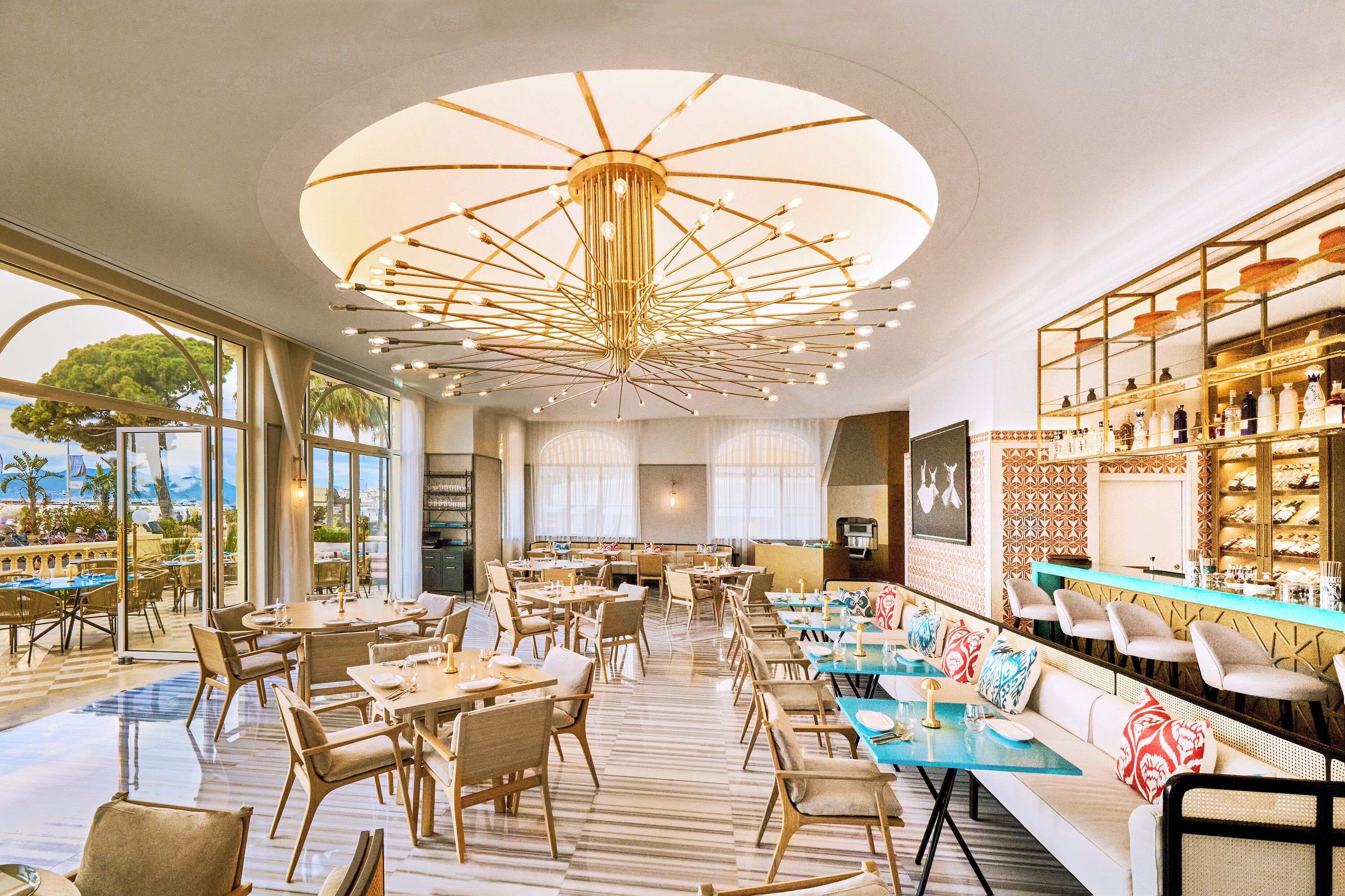Ein geräumiges Restaurant mit einem zentralen Kronleuchter, großen Fenstern mit Blick und einer Bar mit Regalen voller Flaschen.