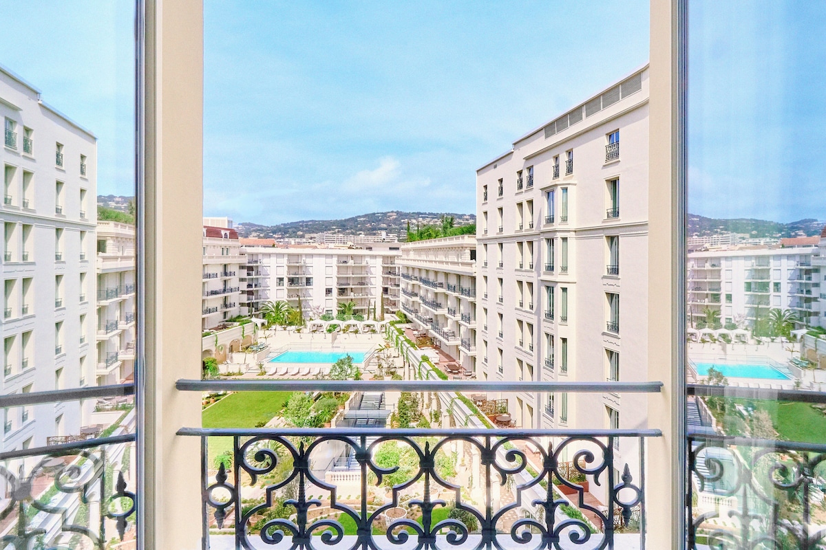 A high-rise hotel with multiple balconies, a swimming pool, and a view of the surrounding cityscape.