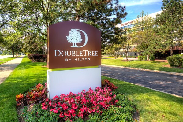 A DoubleTree by Hilton sign with a tree logo, surrounded by well-maintained grass and colorful flowers.