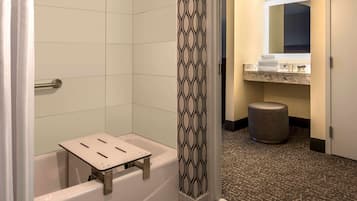 Un baño con una bañera, un taburete pequeño, un perchero y un cubo de basura.