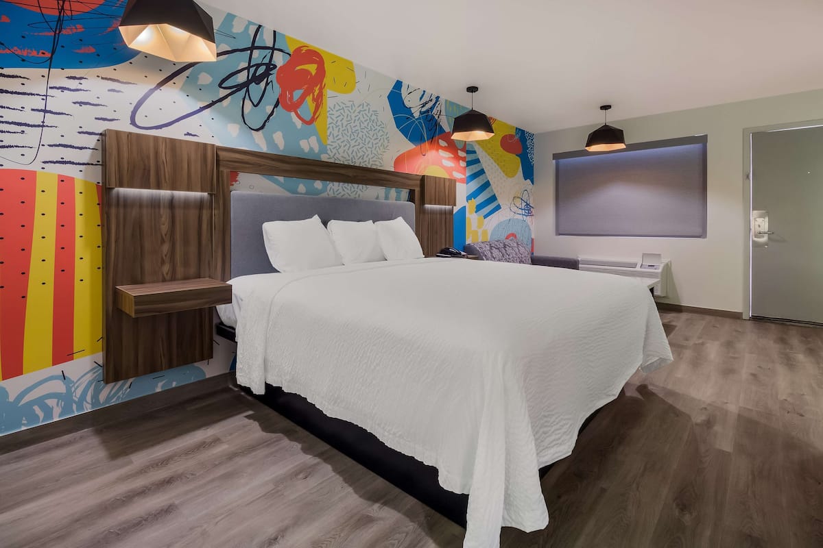 A modern hotel room with a large bed, wooden headboard, and a colorful abstract mural on the wall.