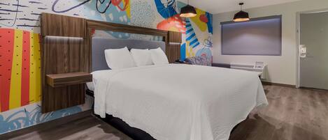 Quarto de hotel moderno com uma cama grande, cabeceira de madeira e um mural abstrato colorido na parede.