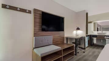 Habitació d'hotel moderna amb paret decorativa de fusta, televisió de pantalla plana, escriptori amb cadira, una banca, taula de nit i mirall.