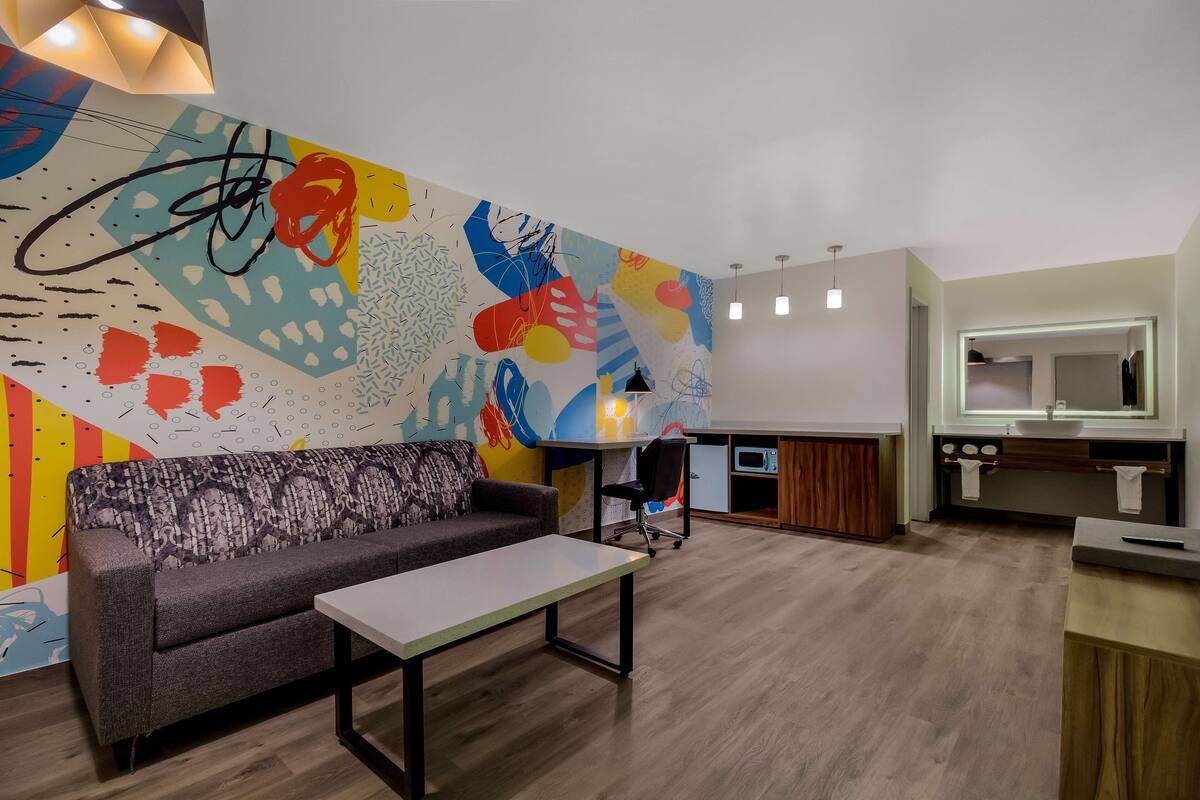 A modern living room with a sofa, a coffee table, and a colorful abstract mural on the wall.