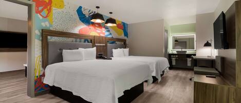 Quarto de hotel com uma cama grande, uma escrivaninha, um espelho e uma televisão.