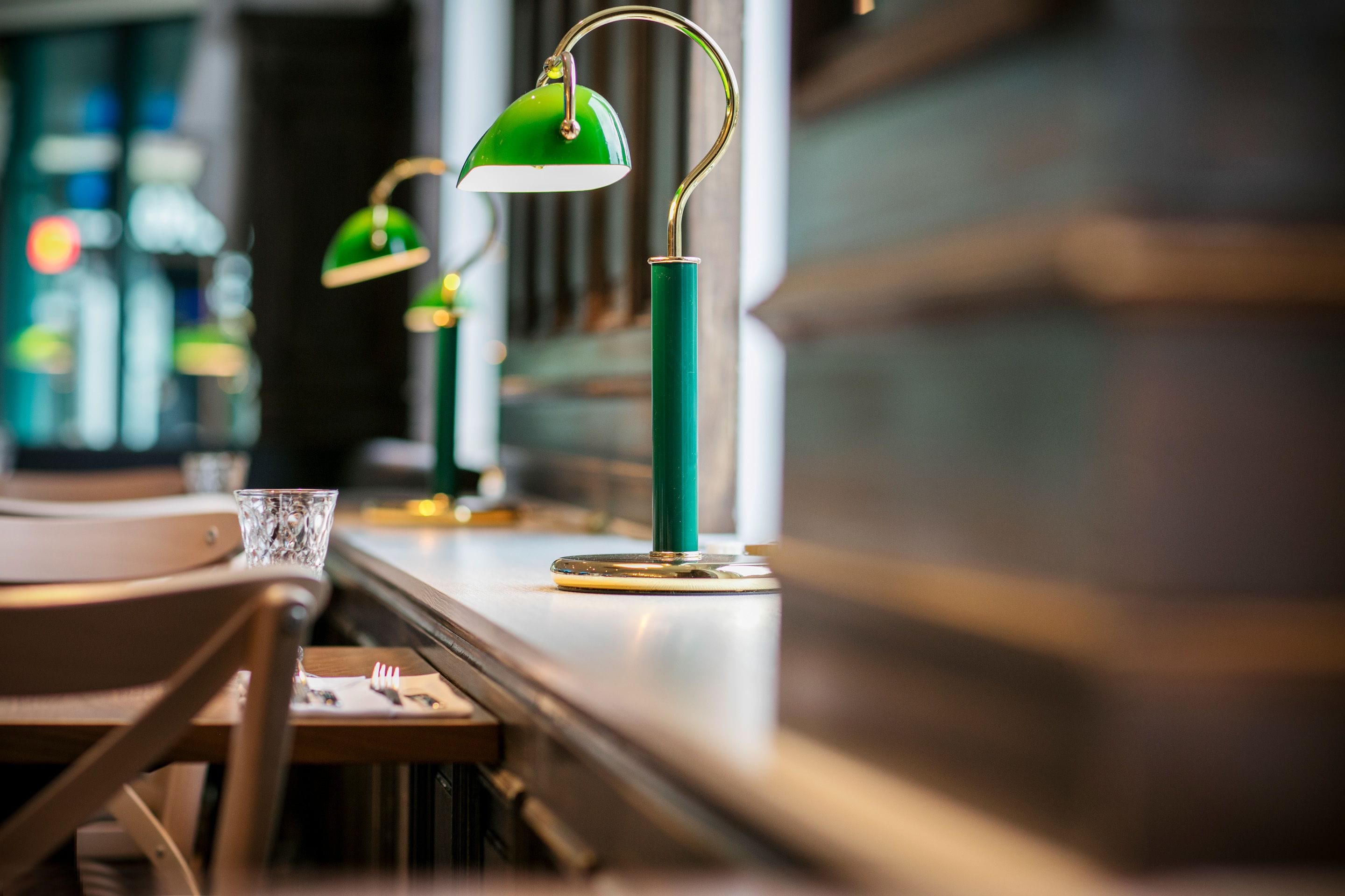 A bar area with green pendant lights, a glass on the counter, and wooden chairs.