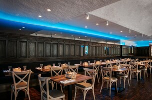 Um restaurante com painéis de madeira nas paredes, várias mesas e cadeiras, e iluminação azul no teto.