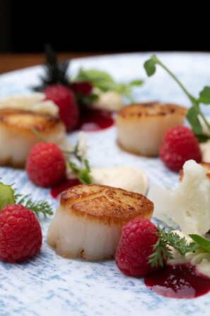 A dessert plate with seared scallops, raspberries, and a dollop of cream.