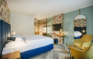 Quarto de hotel com uma cama grande, uma escrivaninha, uma cadeira, um espelho e uma televisão.