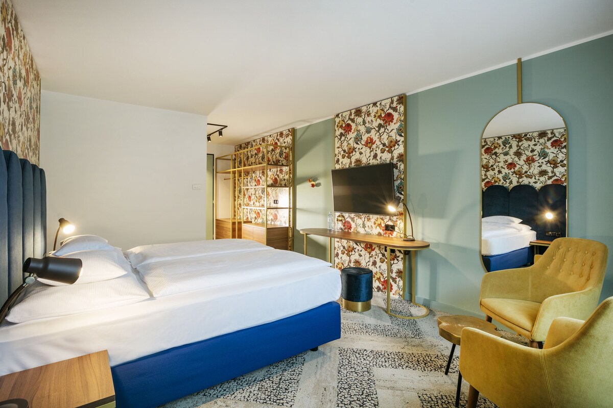 A hotel room with a bed, a desk, a chair, a mirror, and a television.