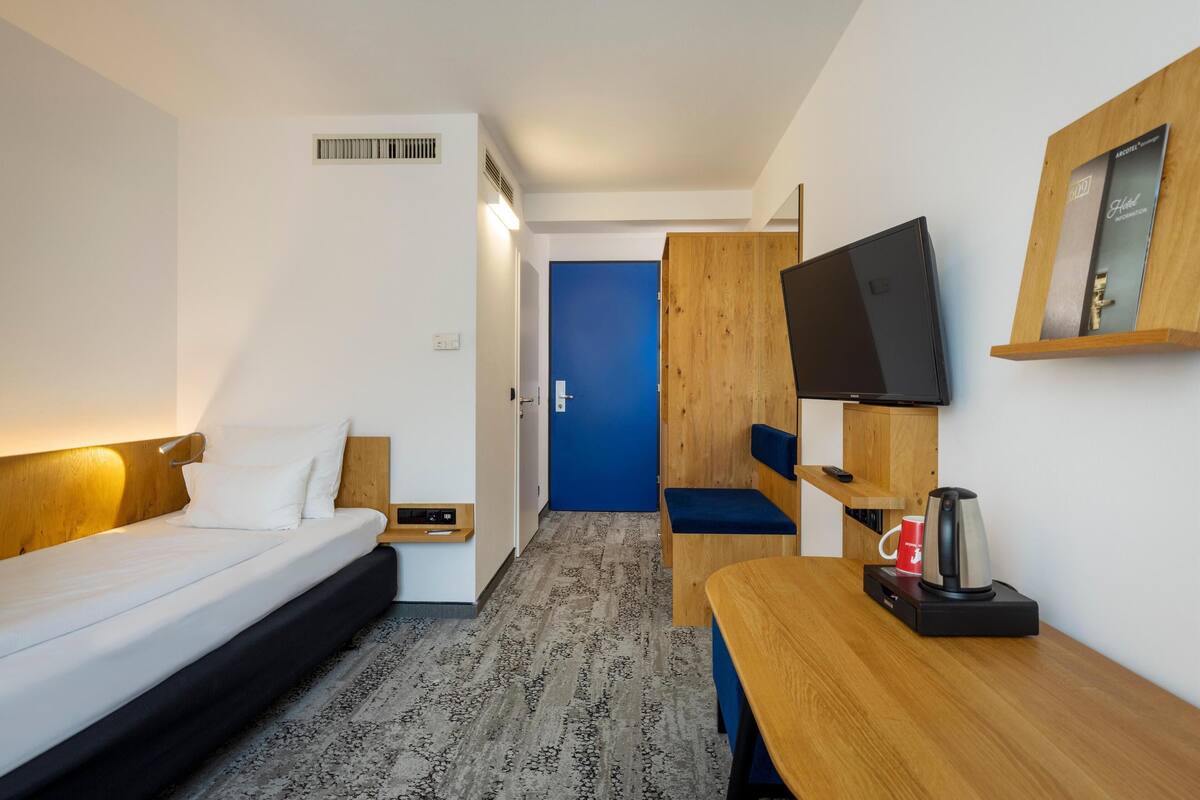 Une chambre d’hôtel avec un lit, un bureau doté d’une machine à café, une télévision et une porte bleue.