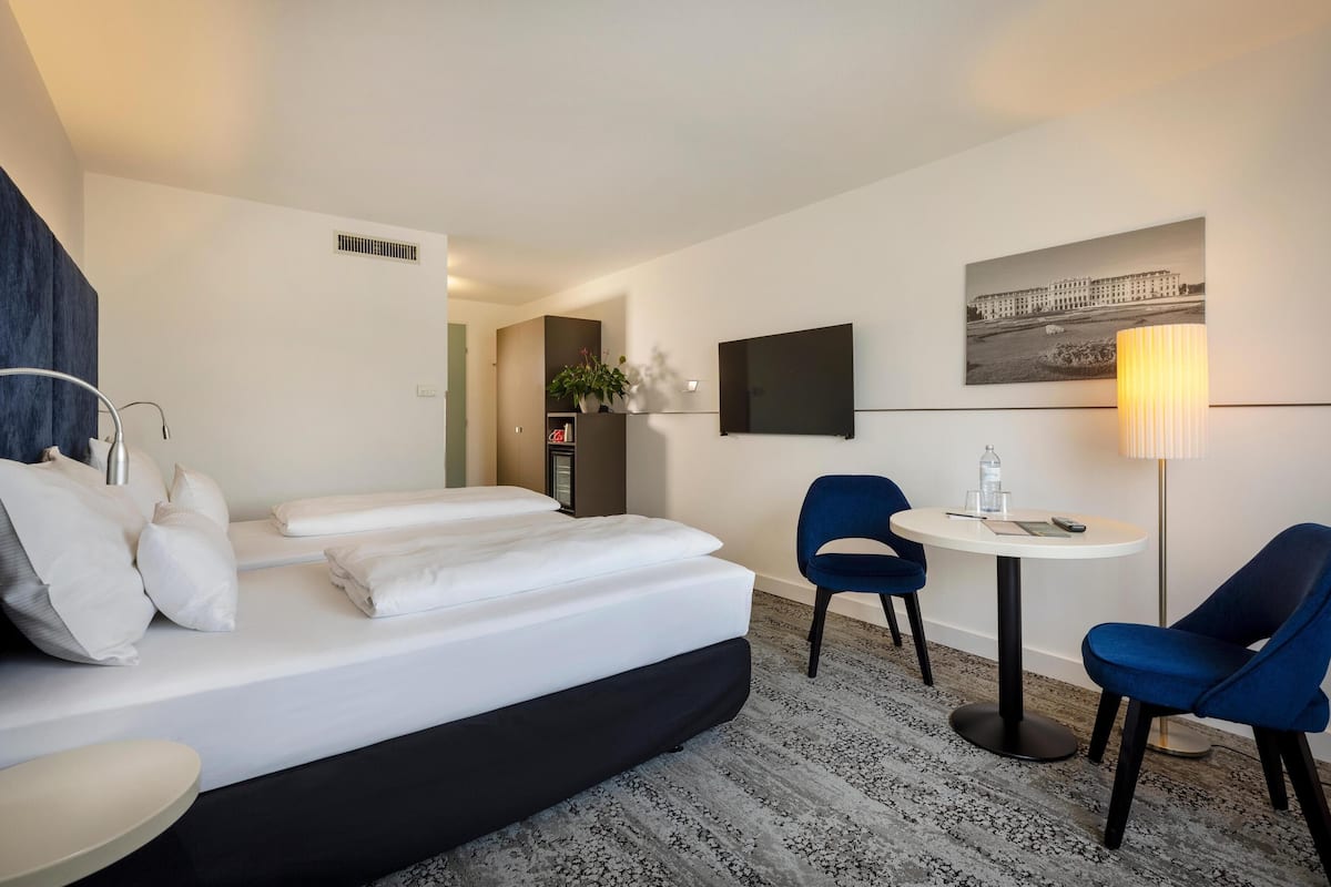 Une chambre d’hôtel avec un lit, deux chaises, une petite table, un téléviseur et une lampe.