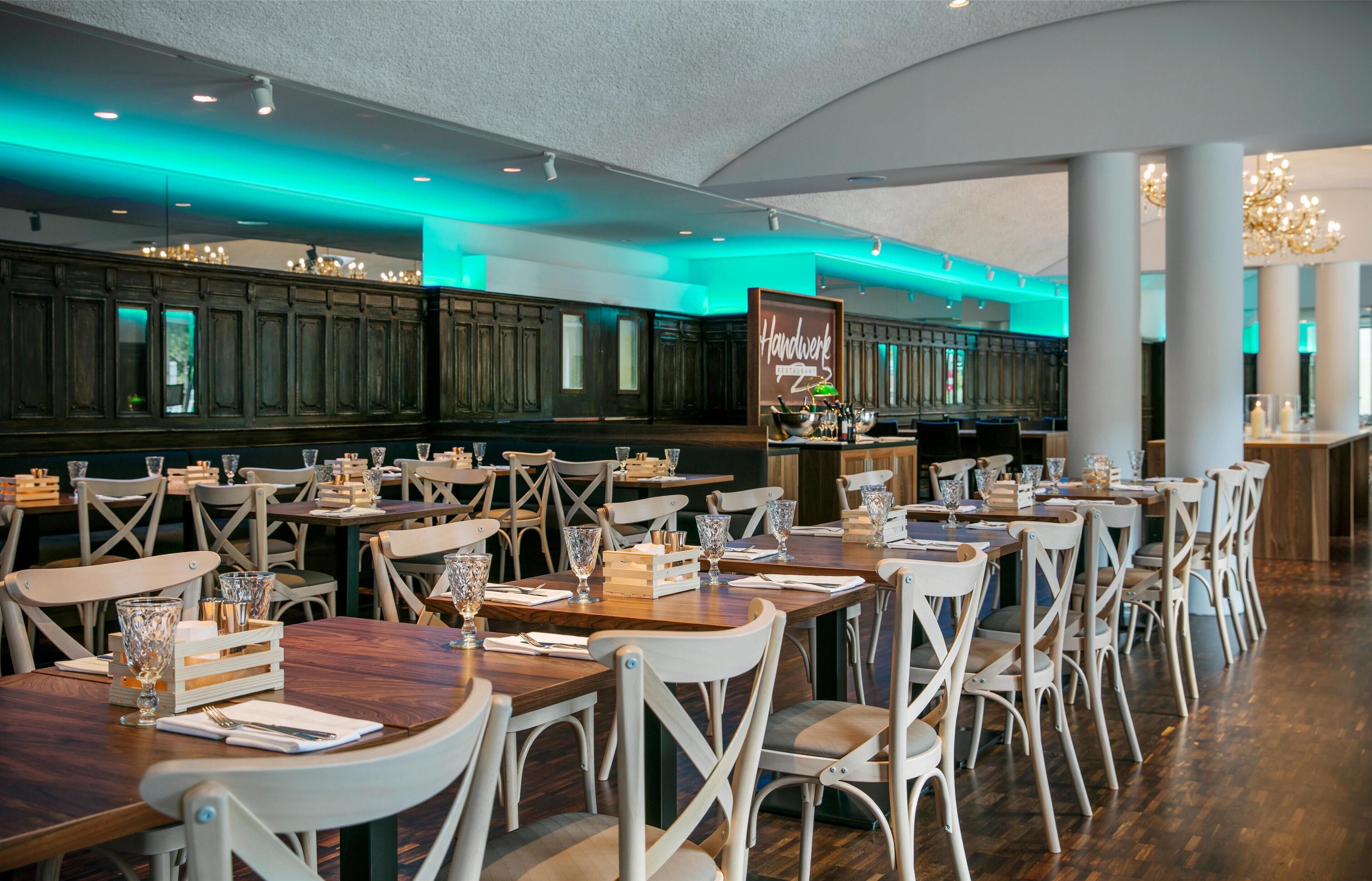 A restaurant with wooden tables and white chairs, teal lighting, and a sign reading "Handwerk".