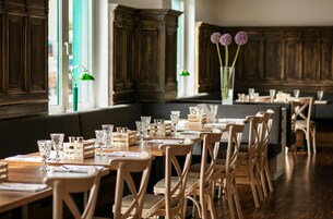 Un ristorante con tavoli e sedie in legno, bicchieri e un vaso con fiori.