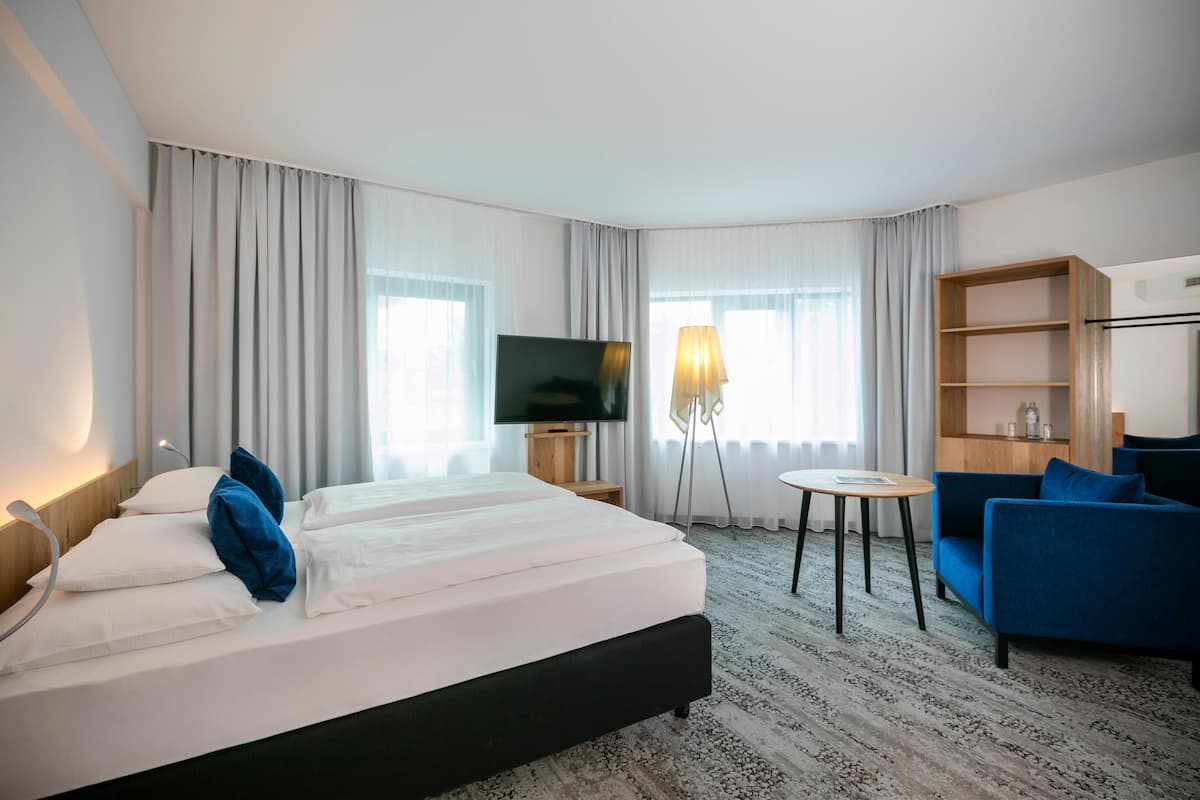 Une chambre d’hôtel avec un grand lit, une télévision, un bureau avec une lampe, un canapé bleu et une bibliothèque.