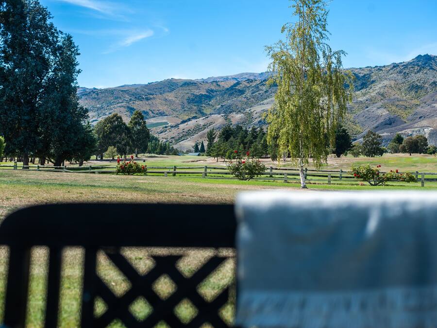 Vista de un parque con una valla de madera, árboles y montañas al fondo.