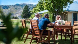 A group of people sitting at an outdoor wooden table with a view of mountains in the background.