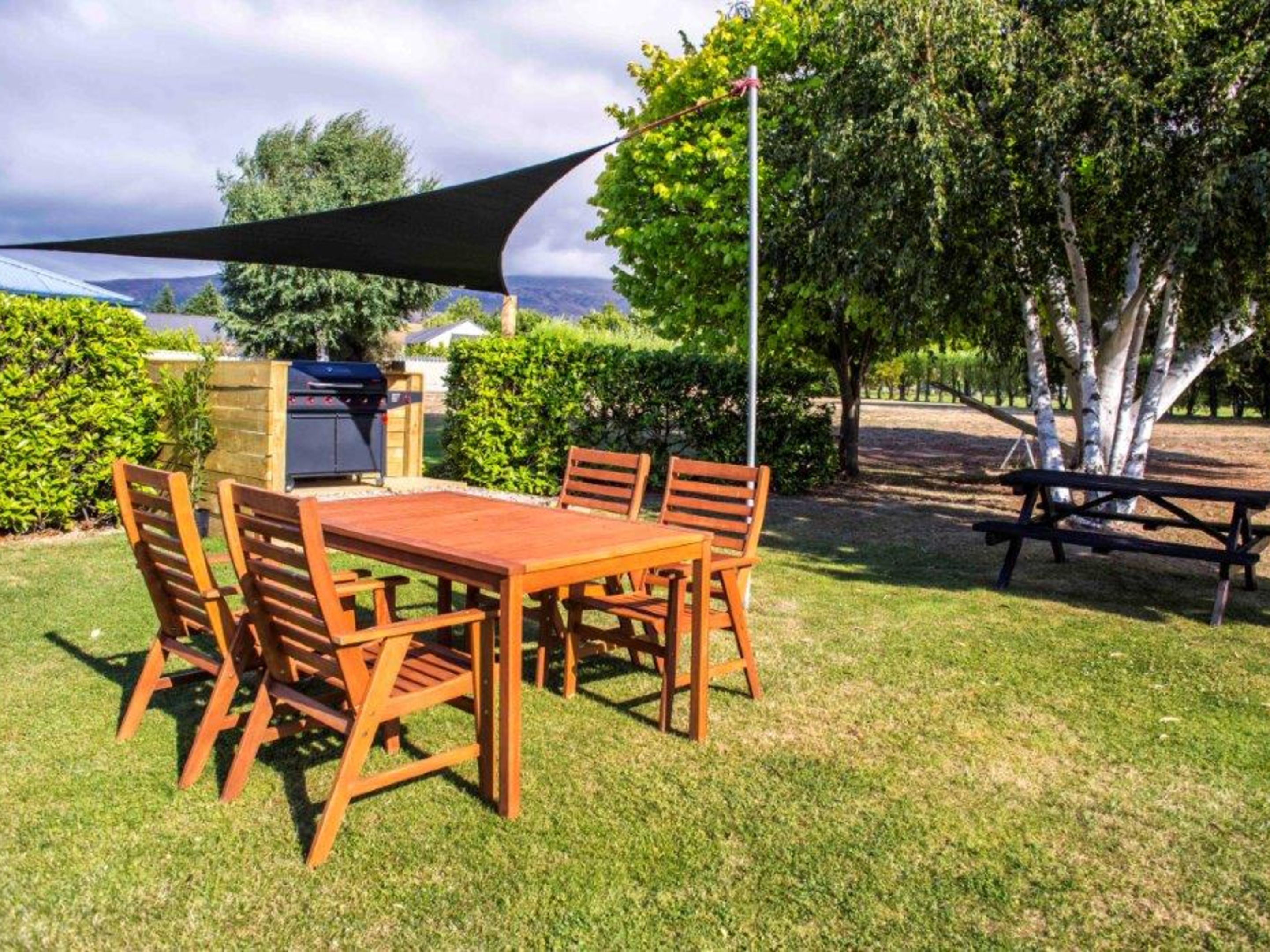 Un área de comedor al aire libre con una mesa y sillas de madera, una parrilla y una mesa de picnic.