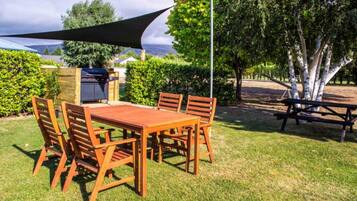 Un área de comedor al aire libre con una mesa y sillas de madera, una parrilla y una mesa de picnic.