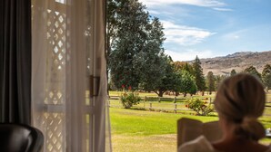A view from a room with a large window overlooking a grassy area with trees and a fence.
