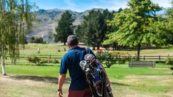 A man carrying golf bags on a golf course with trees and mountains in the background.