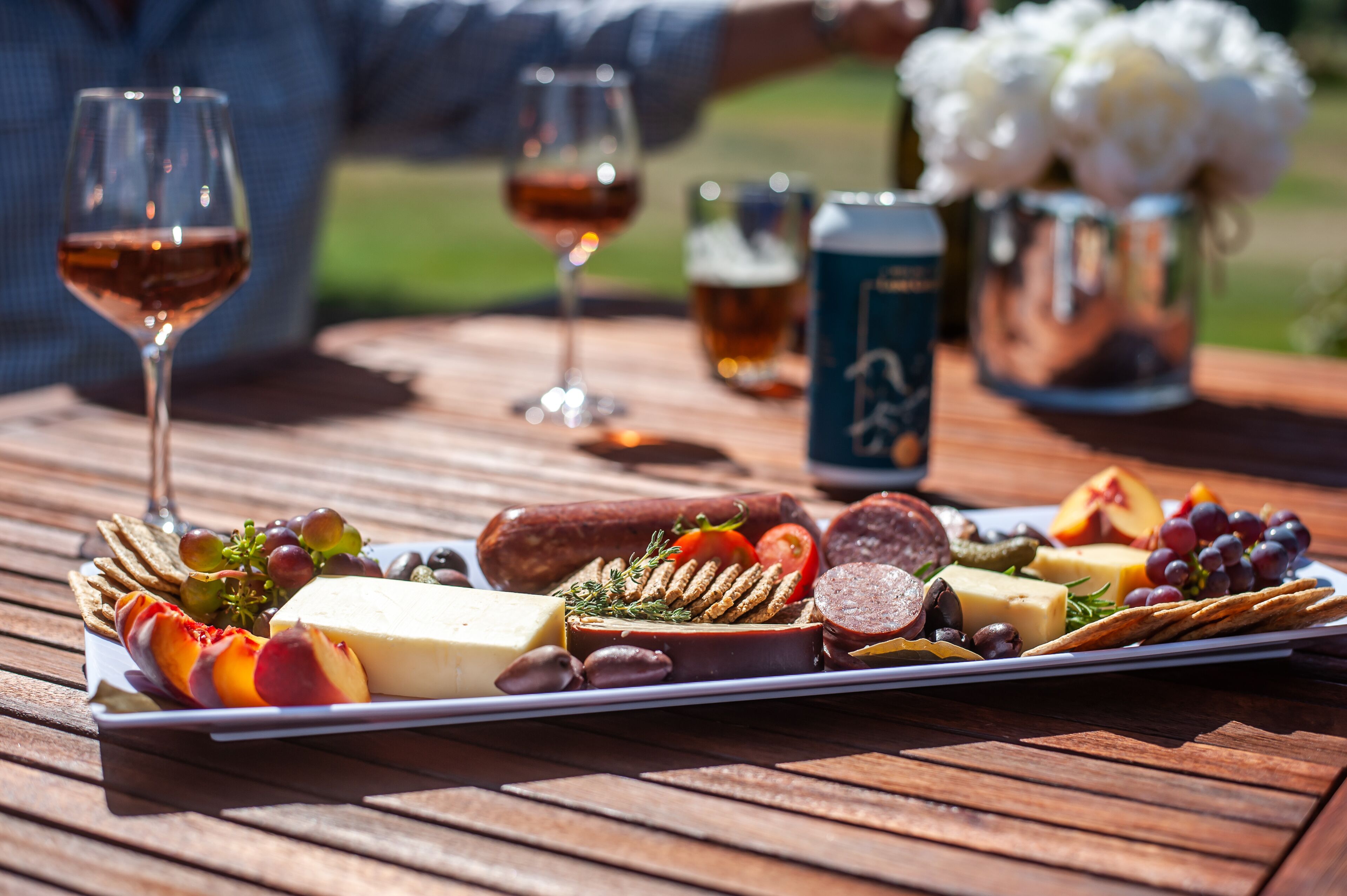 Una mesa de madera con una tabla de embutidos, copas de vino y una jarra de cerveza.