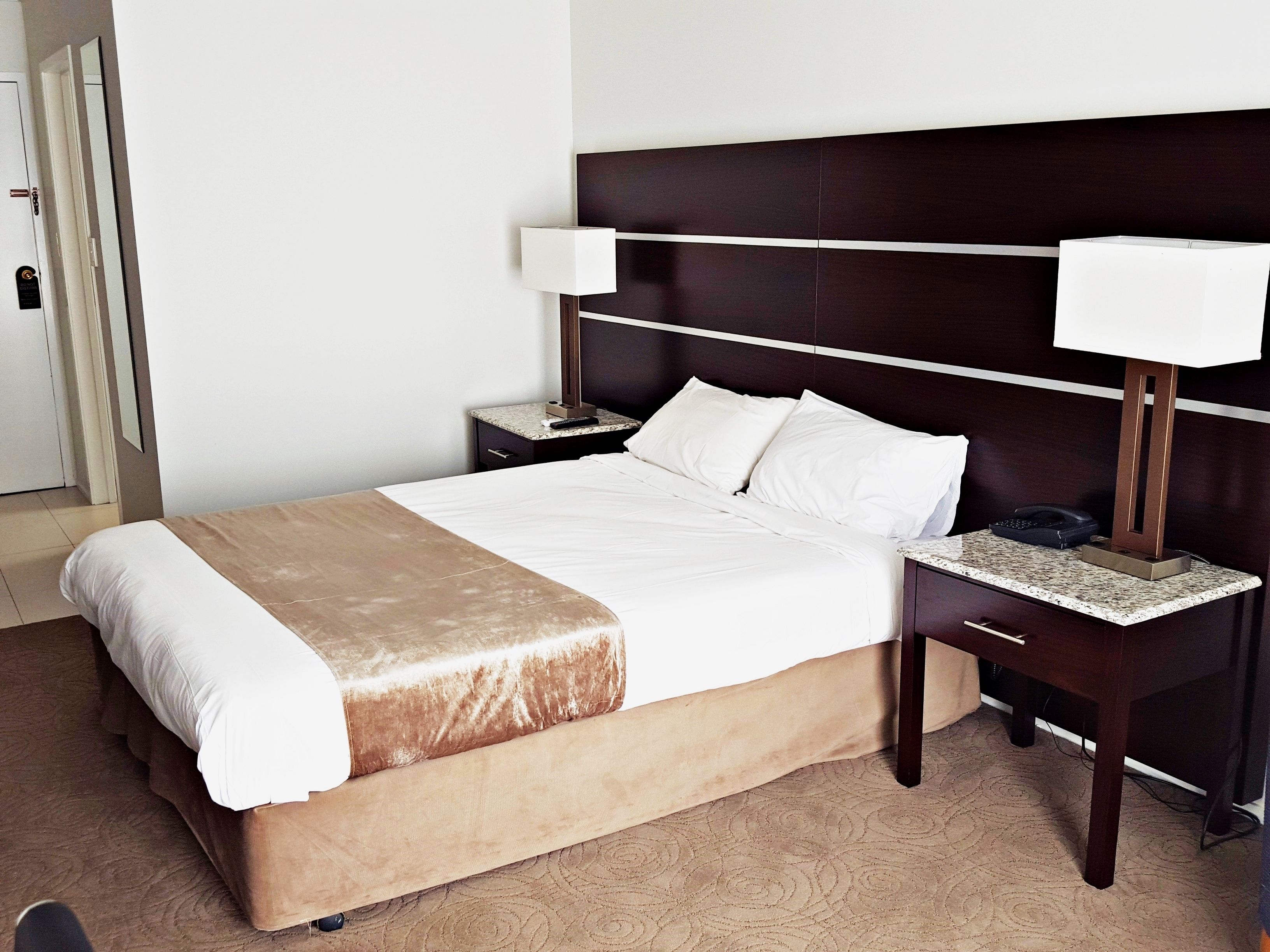 Una habitación de hotel con una cama grande, una mesita de noche, una lámpara y un teléfono.