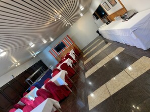 Un salón de conferencias con filas de mesas cubiertas con manteles blancos, un televisor de pantalla plana montado en la pared e iluminación lineal en el techo.