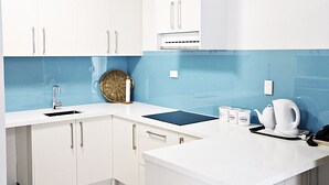 A modern kitchen with white cabinets, a blue backsplash, and a black countertop. - Airport Gateway Hotel (Auckland)
