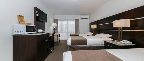 Habitación de hotel con cama, mesitas de noche, escritorio con silla, microondas, televisor y aire acondicionado.