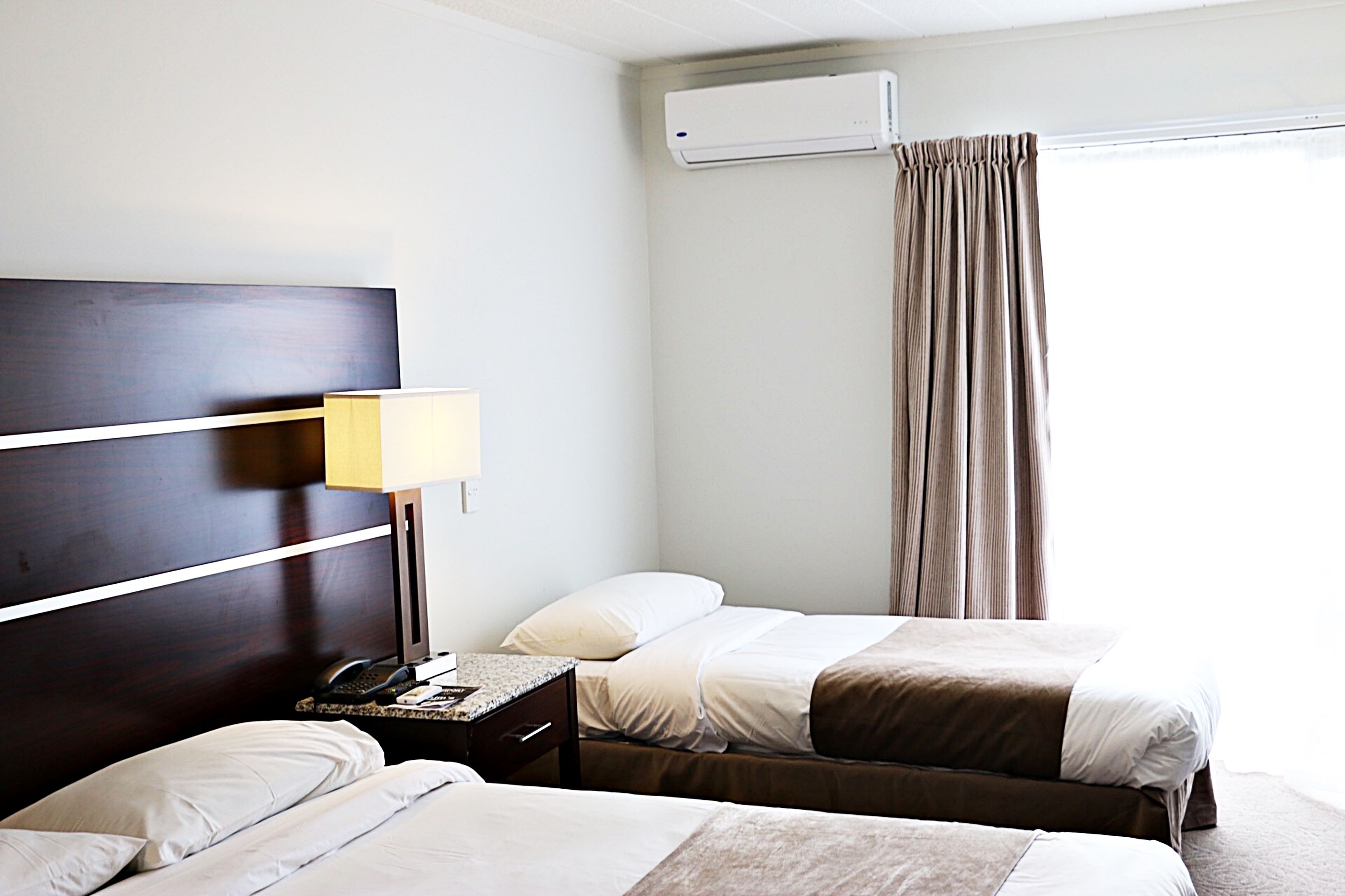 Een hotelkamer met twee bedden, een nachtkastje met een lamp, een telefoon en een airconditioning.