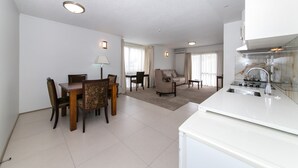 A modern kitchen with white cabinets and a stainless steel sink. There is a dining area with a wooden table and chairs. The living room has a sofa and a coffee table. - Airport Gateway Hotel (Auckland)