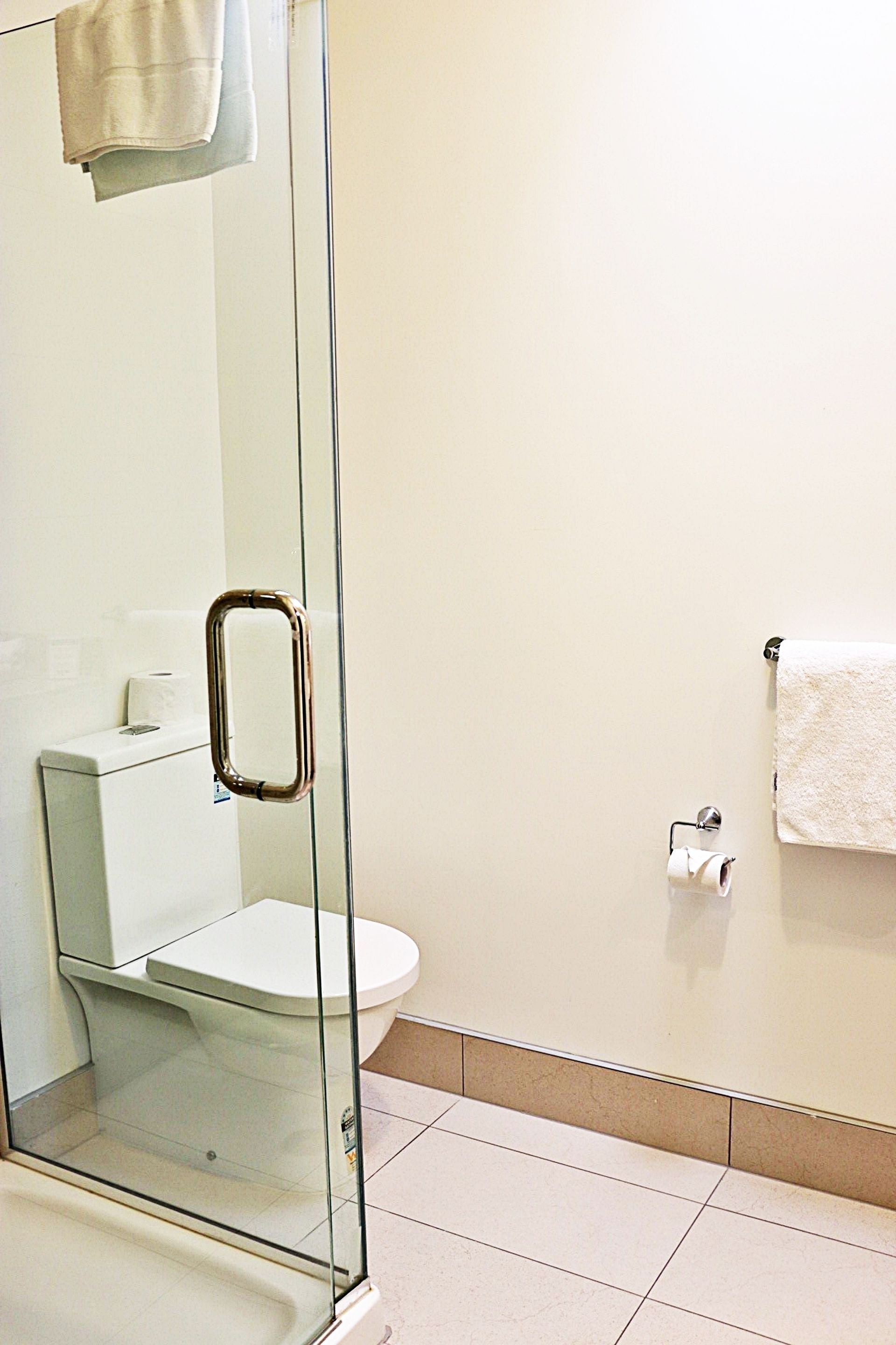 Un baño con cabina de ducha de vidrio, un inodoro y una toalla colgada en la pared.