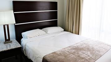 Una cama bien tendida con sábanas blancas y un cabecero oscuro, una lámpara de noche y una ventana con cortinas.