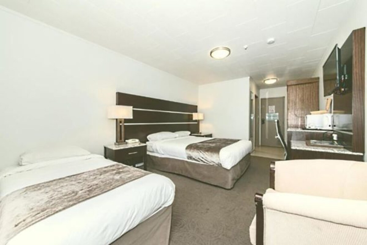 A hotel room with two beds, a desk, a chair, a TV, and a bathroom visible through an open door.