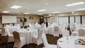 A conference room with multiple round tables, white chairs, and a projector screen. - Airport Gateway Hotel (Auckland)